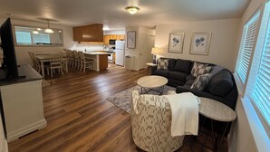 A modern kitchen with wooden cabinets, a dining area with a table and chairs, a living room with a sofa and a coffee table, and a large window with blinds. - Charming 3-bedroom house with AC, WiFi in fantastic Susanville (Susanville)