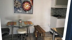 A dining area with a glass table, a chair, a bench, and a painting on the wall.