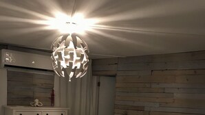 A bedroom with a bed, a dresser, a wooden wall panel, and a hanging light fixture.