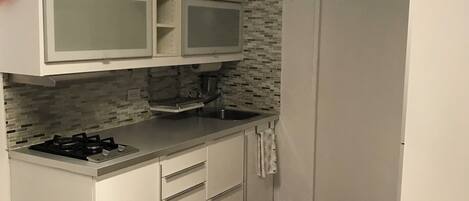 A compact kitchen with white cabinets, a gas stove, a sink, and a red rug.