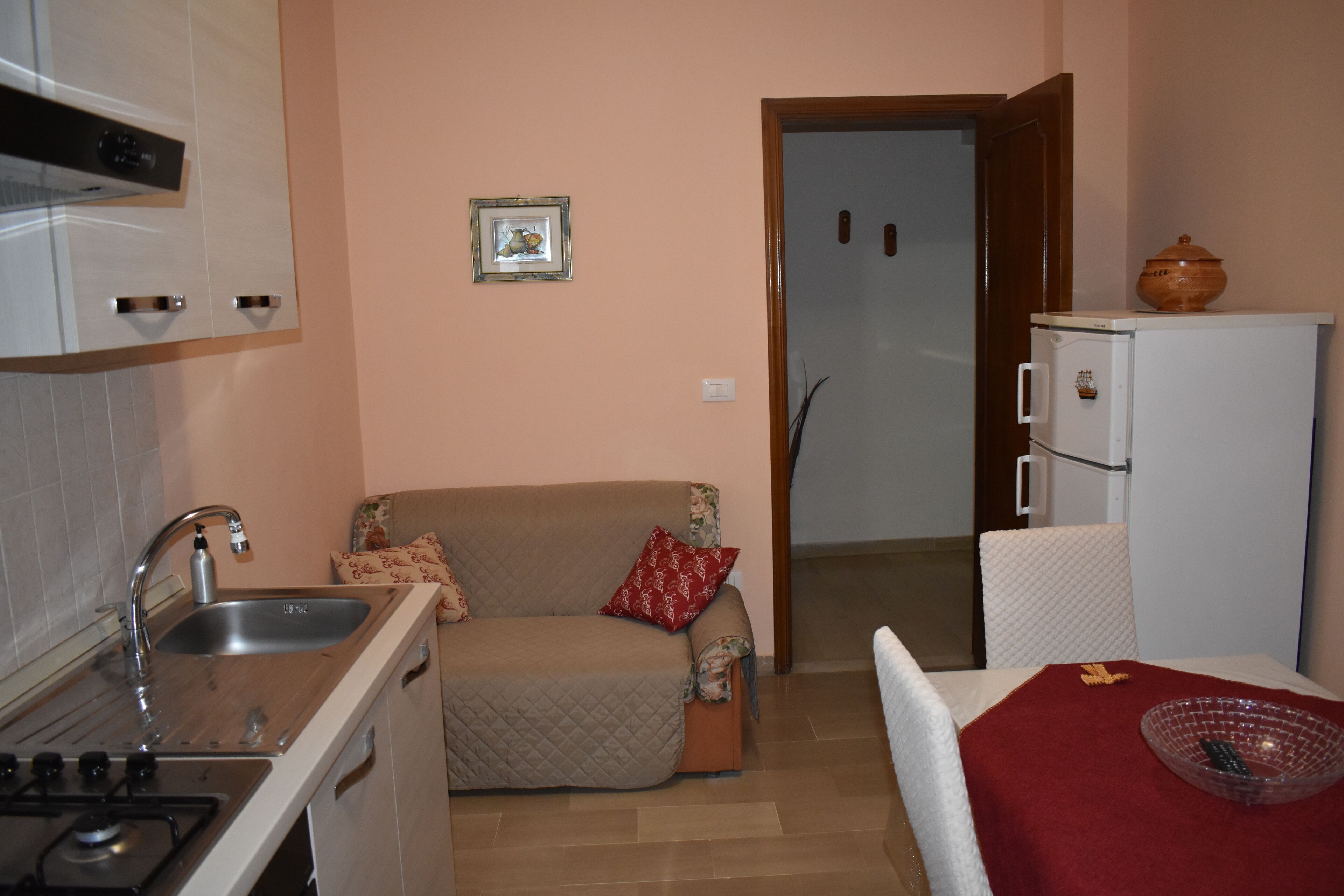 Eine kleine Küche mit Spüle, Herd und kleinem Kühlschrank. Ein Sofa mit gesteppter Hülle und dekorativen Kissen lehnt an der Wand.