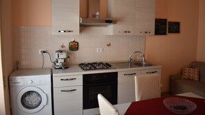 A compact kitchen with a washing machine, stove, oven, and sink. - Naxos Sea Apartment (Giardini Naxos)