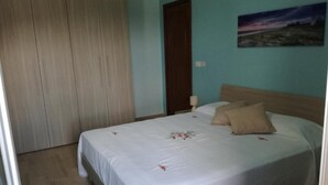 A bedroom with a bed, a nightstand, a wooden wardrobe, and a door. - Naxos Sea Apartment (Giardini Naxos)