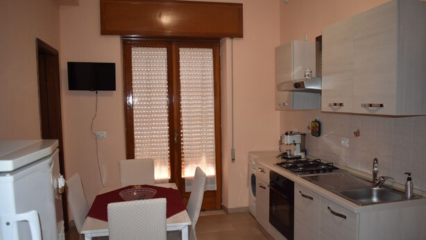 A compact kitchen with a dining area, a washing machine, and a TV mounted on the wall. - Naxos Sea Apartment (Giardini Naxos)