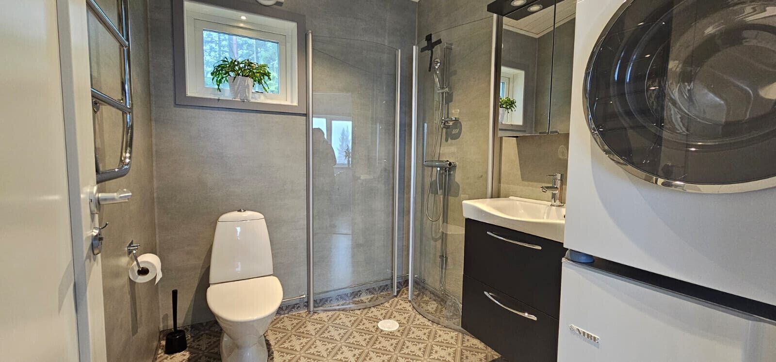 Een badkamer met toilet, douche, wastafel en een raam met een plant.