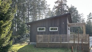 Een houten chalet met twee ramen, een terras en een bos op de achtergrond.