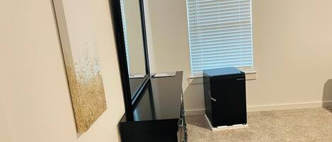 A room with a black dresser, a mirror, a framed picture on the wall, and a window with blinds.