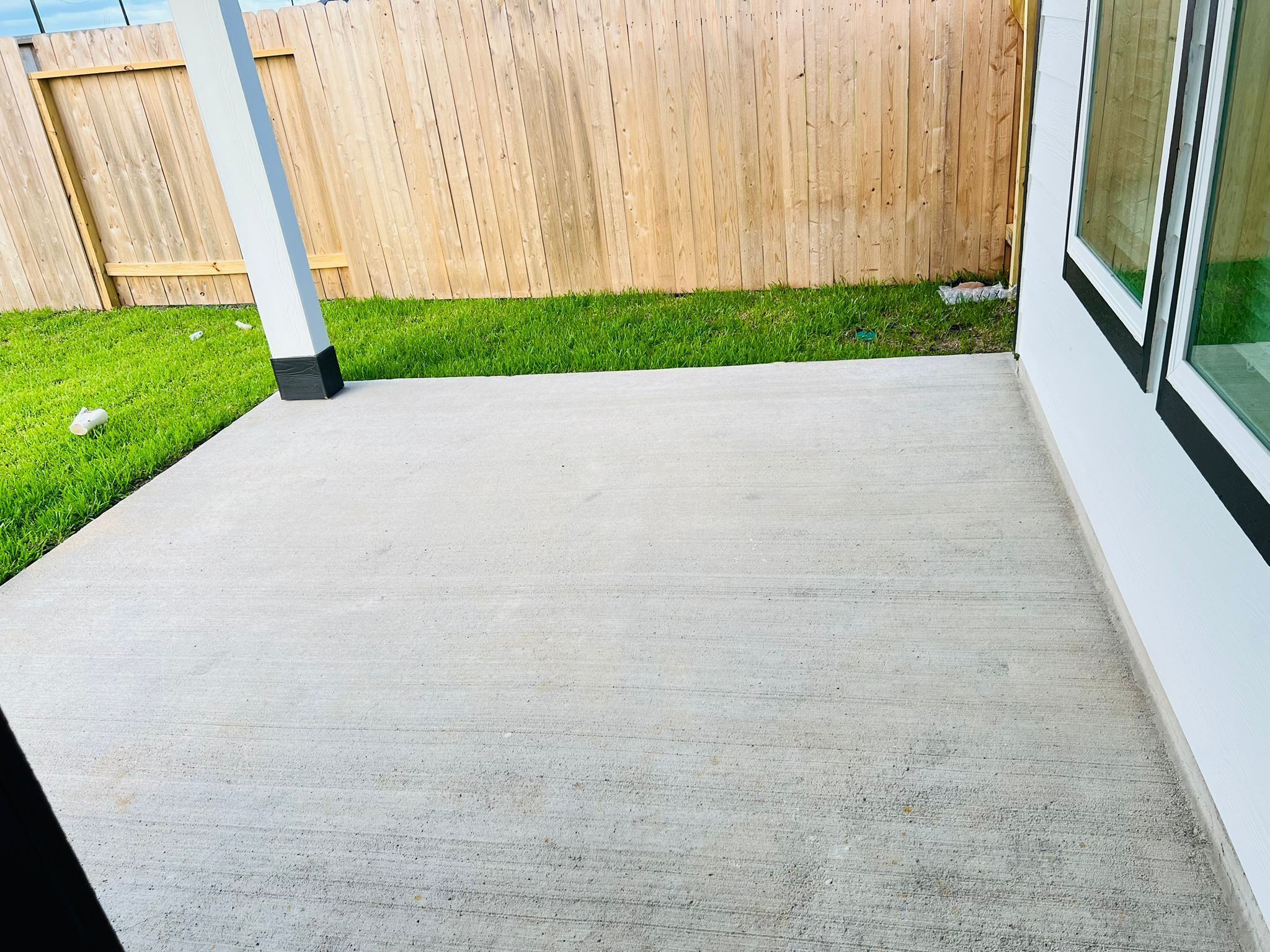 Une terrasse en béton, avec une clôture en bois et une pelouse verdoyante en arrière-plan.