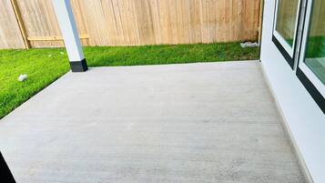 Une terrasse en béton, avec une clôture en bois et une pelouse verdoyante en arrière-plan.