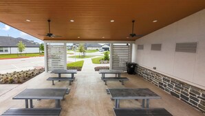 Ett takförsett utomhusområde med sittplatser och bänkar, med utsikt över en bostadsgata.