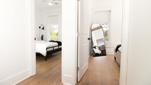 A bedroom with a bed, a standing mirror, a ceiling fan, and a window with a view of greenery. - Modern Loft in Lively SoMa Downtown (Little Rock)