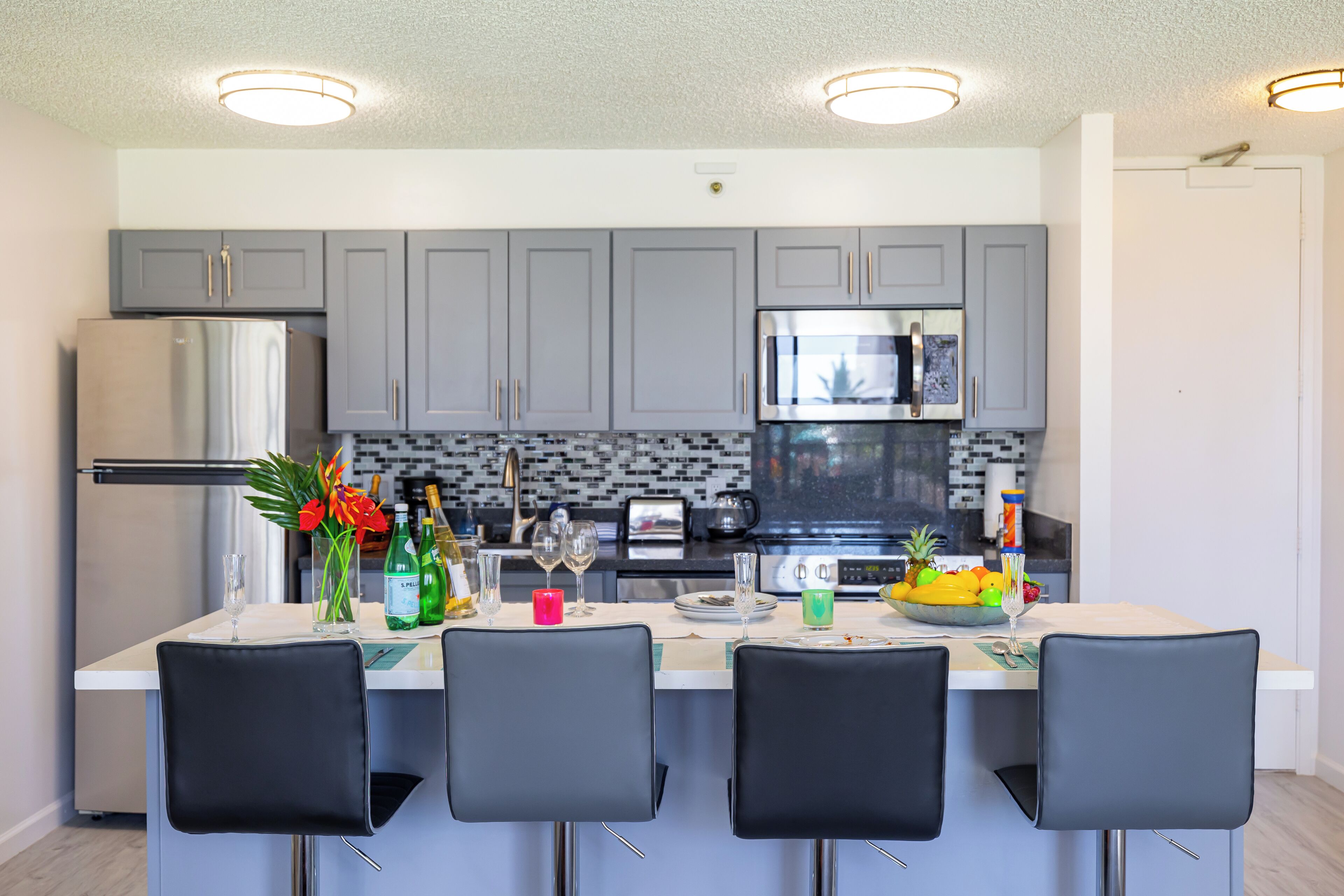A modern kitchen with grey cabinets, stainless steel appliances, and a central island with bar stools.