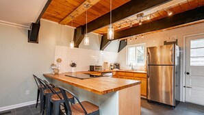 A modern kitchen with a wooden island, stainless steel appliances, and hanging pendant lights. - 3-bed, charming modernized cottage tucked into wooded hillside in Deep Creek, MD (Oakland)