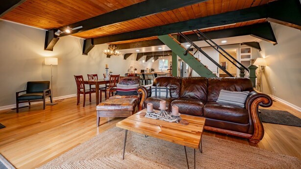 A spacious living room with a wooden ceiling, a leather sofa, a coffee table, and a staircase leading to an upper level. - 3-bed, charming modernized cottage tucked into wooded hillside in Deep Creek, MD (Oakland)