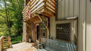 A wooden deck with a bench, a stone wall, and a window with blinds. - 3-bed, charming modernized cottage tucked into wooded hillside in Deep Creek, MD (Oakland)