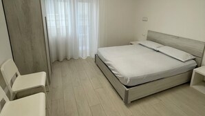 A bedroom with a bed, a chair, a nightstand, and a window with curtains.