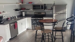 A compact kitchen with white cabinets, a stainless steel refrigerator, a microwave, and a stove. There is a round wooden table with four chairs. - Remodeled downtown studio with remarkable views! (Luverne)