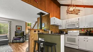A modern kitchen with white cabinets, a microwave, and an oven. There is a wooden island with bar stools, and a staircase leading to a lofted area.