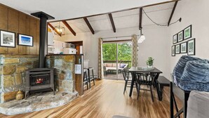 A cozy room with a stone fireplace, a dining area, and a view through a glass door to an outdoor deck.