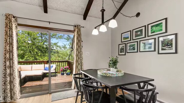 A dining area with a table, chairs, a potted plant, and a view of a deck with outdoor furniture.