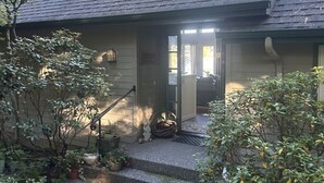 A house with a sloped roof, a porch with steps, and a small garden area with potted plants and a statue. - Stunning Waterfront Retreat In Port Madison, Bainbridge Island-Furnished (Bainbridge Island)