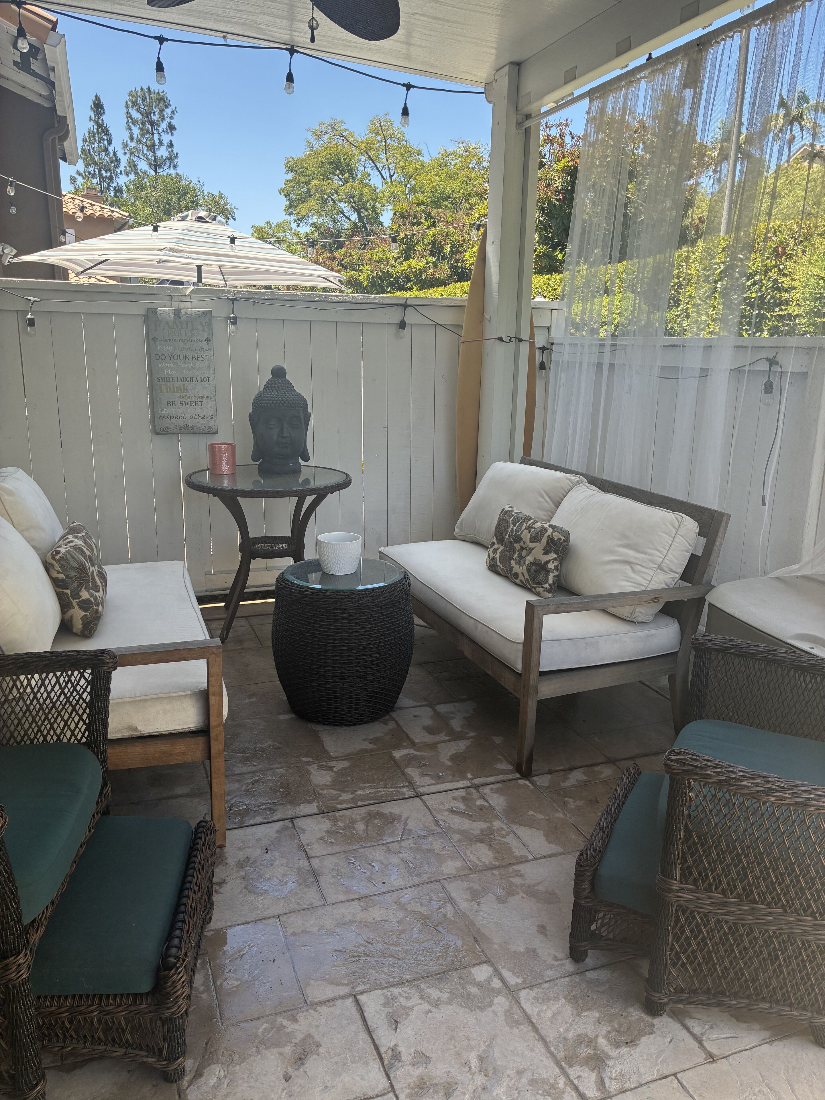 A covered patio area with wicker furniture, a table with a Buddha statue, and a sign with family values.