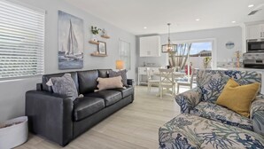 Een moderne woonkamer met een zwarte leren bank, een fauteuil met een patroon en een eethoek met een witte tafel en stoelen.