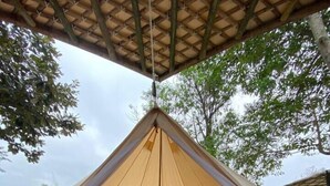A large, open-sided tent with a central bed and a wooden floor.