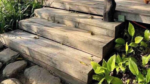 A wooden deck with steps leading to a covered area, surrounded by potted plants and outdoor furniture.