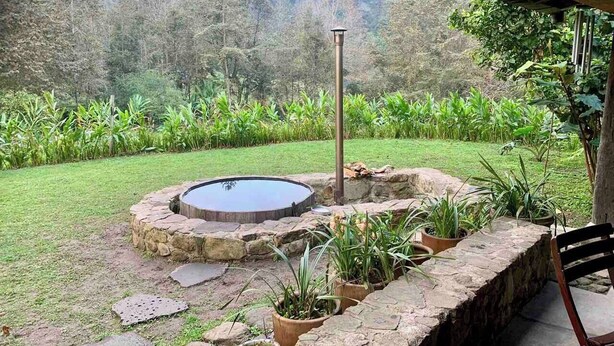 Un bain à remous en pierre, entouré de plantes en pot, situé dans un jardin avec vue sur une zone boisée.