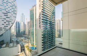 Un immeuble de grande hauteur doté d’une façade en verre, de nombreux balcons et offrant une vue sur un paysage urbain composé d’autres bâtiments et d’une piscine.