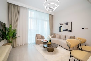 Un salon moderne avec un canapé, des fauteuils, une table basse et une grande fenêtre agrémentée de rideaux.
