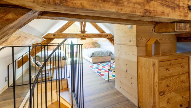 A loft bedroom with a wooden staircase, a bed, a dresser, and a colorful rug. - CASSANOS - CHANAZ - Gîte (CHANAZ)