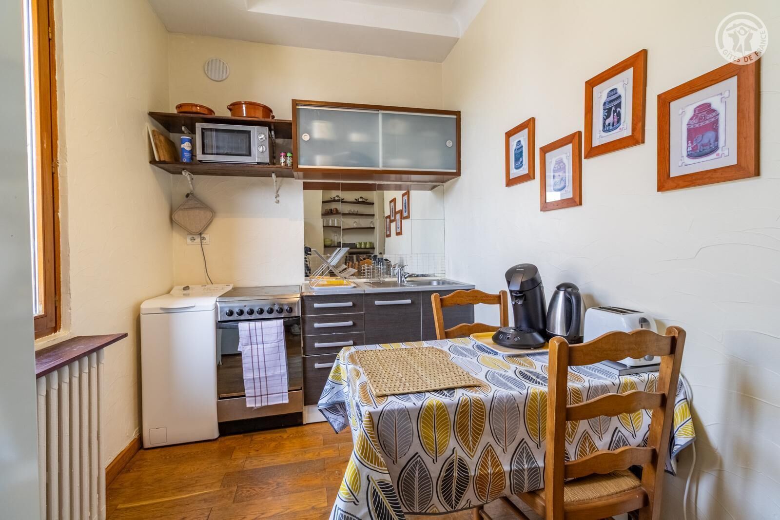A compact kitchen with a stove, microwave, and coffee maker. There is a dining table with chairs and a window.