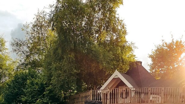 A two-story wooden cabin with a deck, surrounded by dense greenery. - Stunning Tiny House w/ Outdoor Tub & Views (Pontsticill)