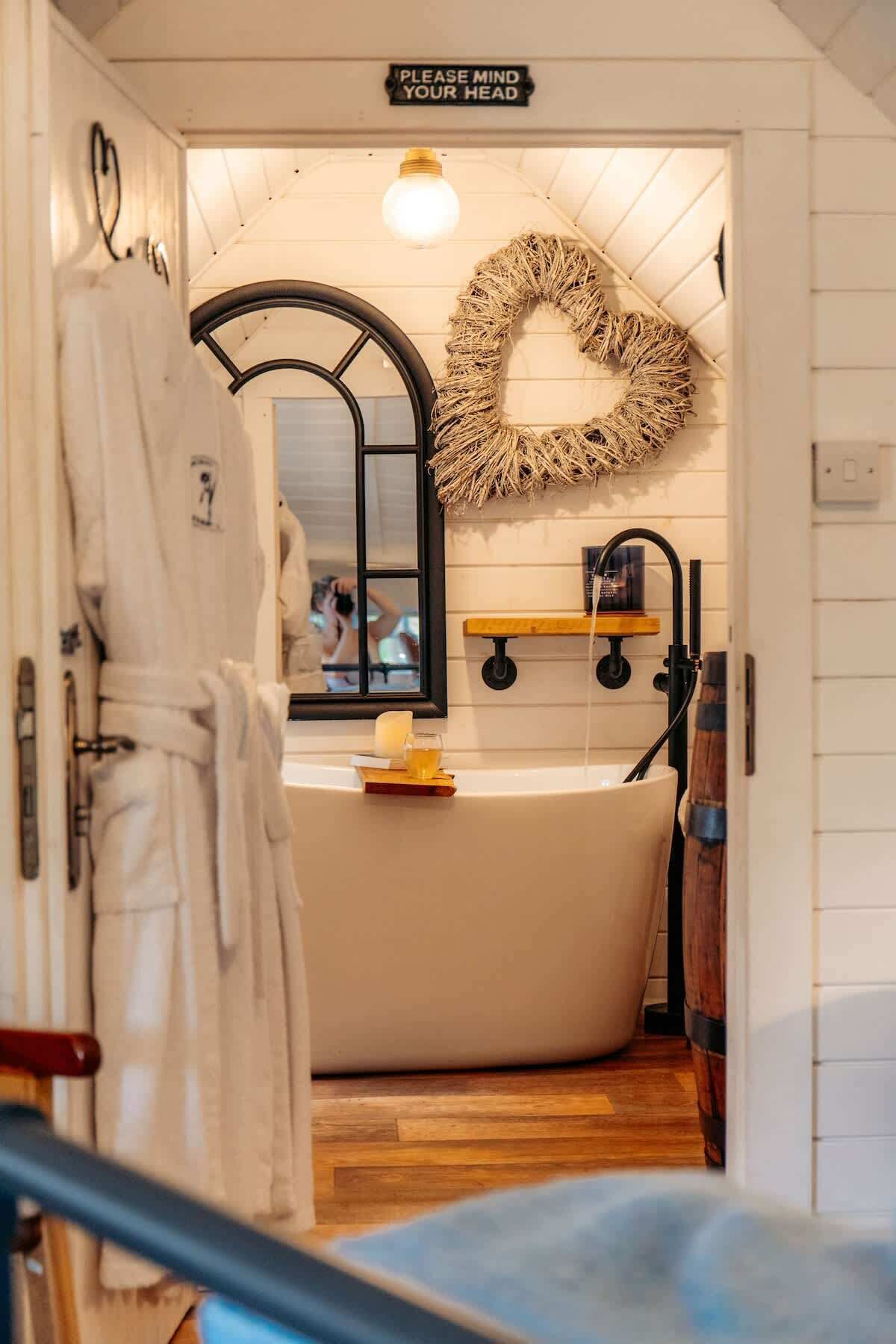 A bathroom with a bathtub, a mirror, a towel rack, and a sign that says "PLEASE MIND YOUR HEAD".