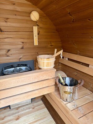 Una sauna de madera con bancos, un balde de madera, un termómetro y una jarra de champán.