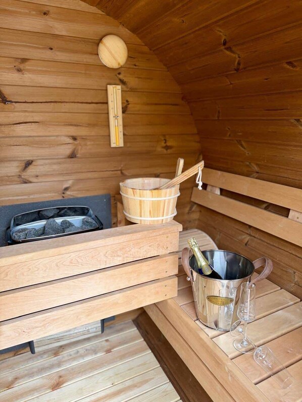 A wooden sauna with benches, a wooden bucket, a thermometer, and a bucket of champagne.