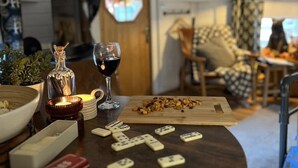 A cozy living room with a wooden table set for dominoes, a wine glass, and a candle. - Stunning Tiny House w/ Outdoor Tub & Views (Pontsticill)