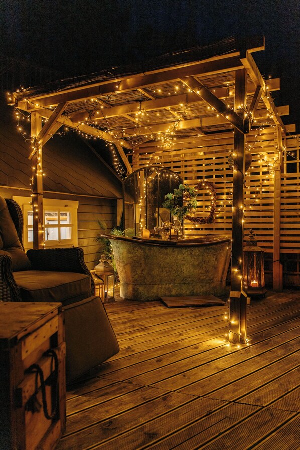 An outdoor wooden deck with a stone fountain, string lights, and a wooden pergola.