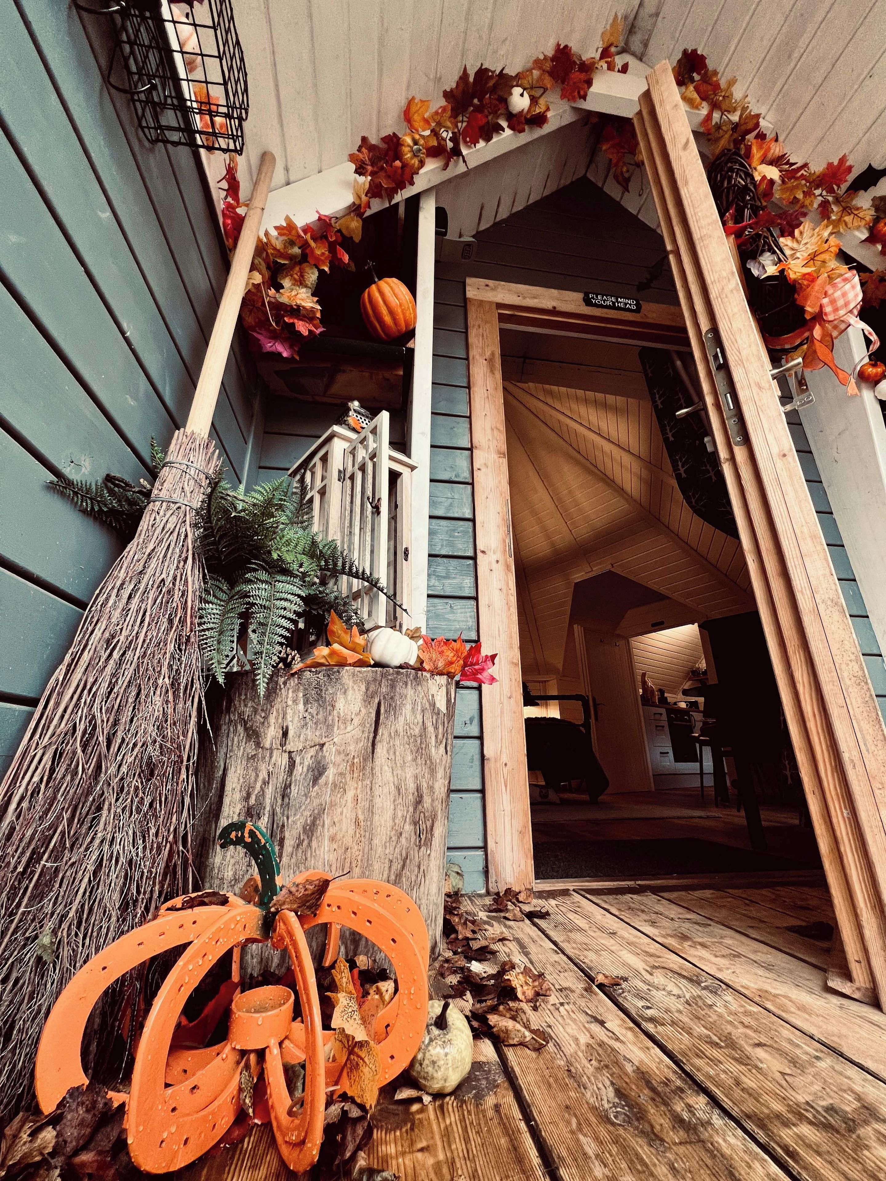 A wooden porch with a broom, pumpkins, and autumn leaves.