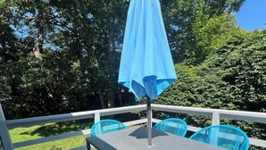 Eine Terrasse mit Tisch und Stühlen, einem blauen Sonnenschirm und Blick auf Bäume.
