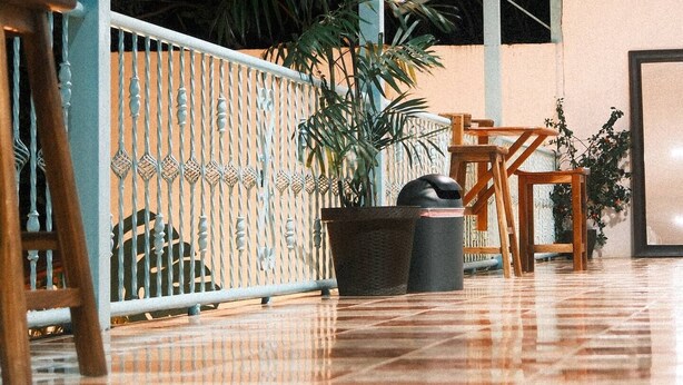 Un espacio interior amplio con suelo de baldosas, una escalera de madera, barandilla metálica y varias plantas en macetas.