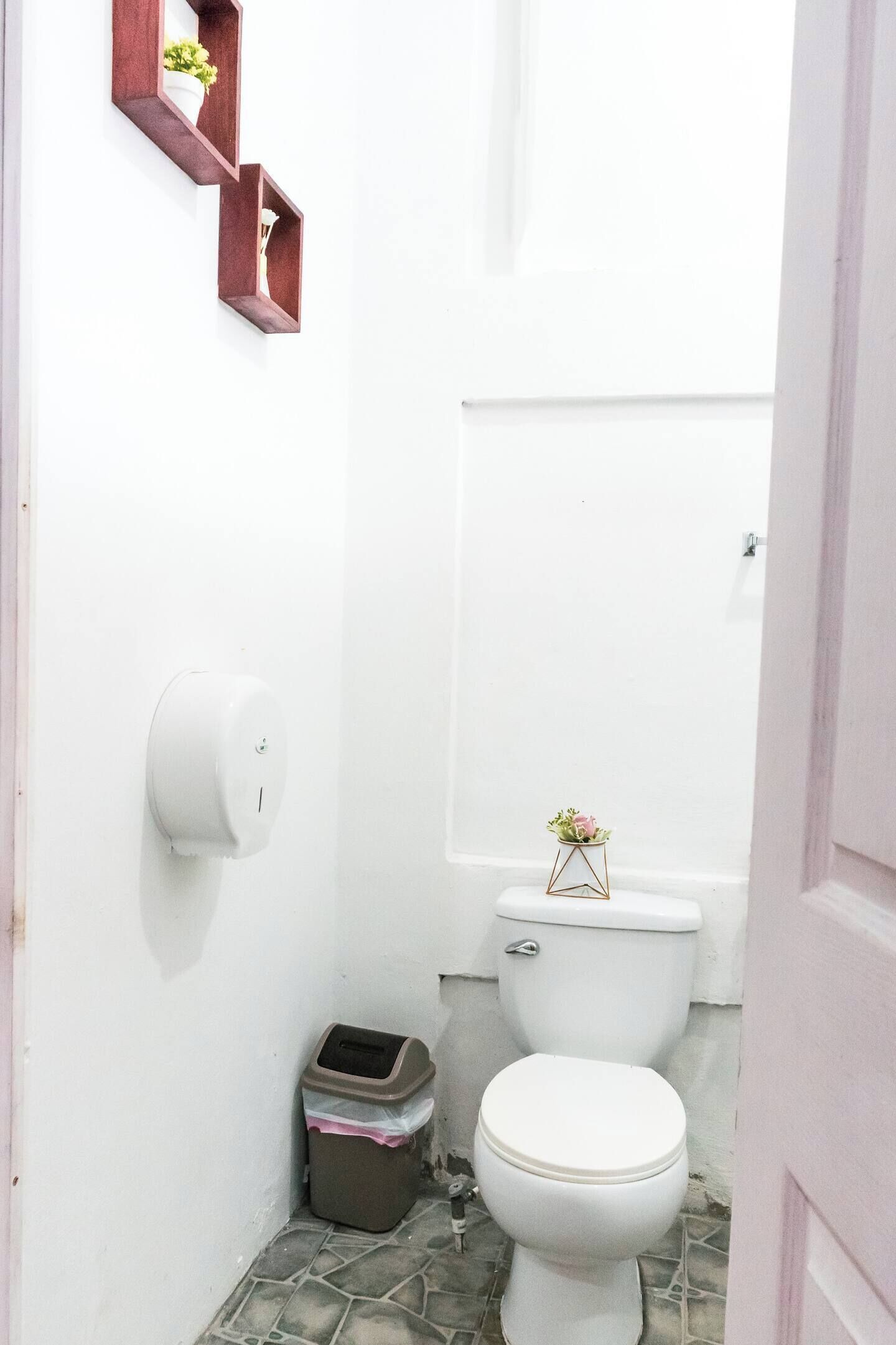Un baño pequeño con un inodoro, un cesto de basura y un sujetapapeles en la pared.