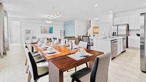 A modern kitchen with white cabinets, stainless steel appliances, and a dining area with a wooden table set for six.