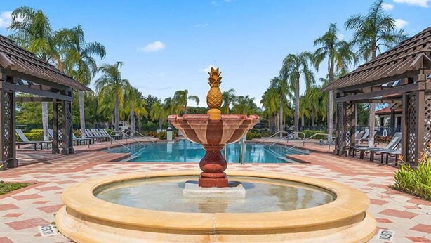 A pool area with a central fountain, lounge chairs, and palm trees.