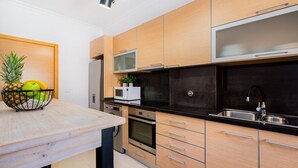 Een moderne keuken met houten kastjes, een zwart aanrecht, roestvrijstalen apparatuur en een fruitschaal op de tafel.