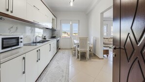 Een moderne keuken met witte kastjes, een inbouwmagnetron en een eethoek met een tafel en stoelen.