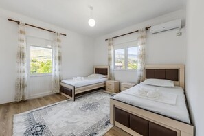 Une chambre avec deux lits, une grande fenêtre, un luminaire au plafond et un appareil de climatisation.