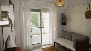 A living room with a sofa, a small table, a TV, and a curtain-covered sliding door leading to a balcony. - Anacasa Royal Playa les Marines AP1213 (Denia)